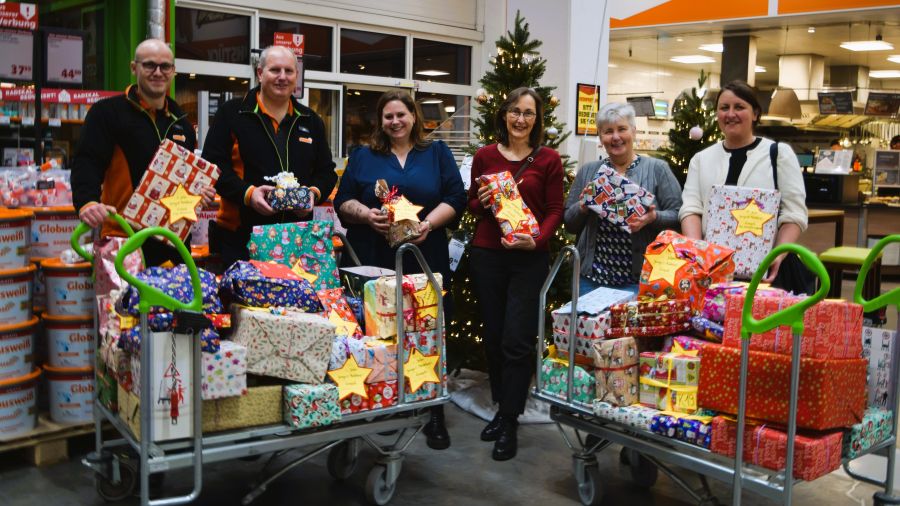 Das Foto zeigt die Mitarbeitenden von Globus Baumarkt und Caritas mit zwei großen Transportwagen voller Geschenke, alle halten ein Geschenk in der Hand.