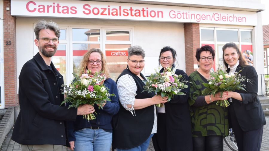 Das Bild zeigt ein Gruppebild mit Blumensträußen vor der Caritas-Sozialstation Göttingen / Gleichen.