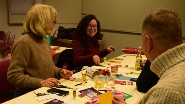 Das Bild zeigt drei Menschen an einem Tisch, wie sie Weihnachtskarten basteln.